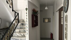 Un couloir avec un escalier en marbre, un extincteur et une horloge au mur.