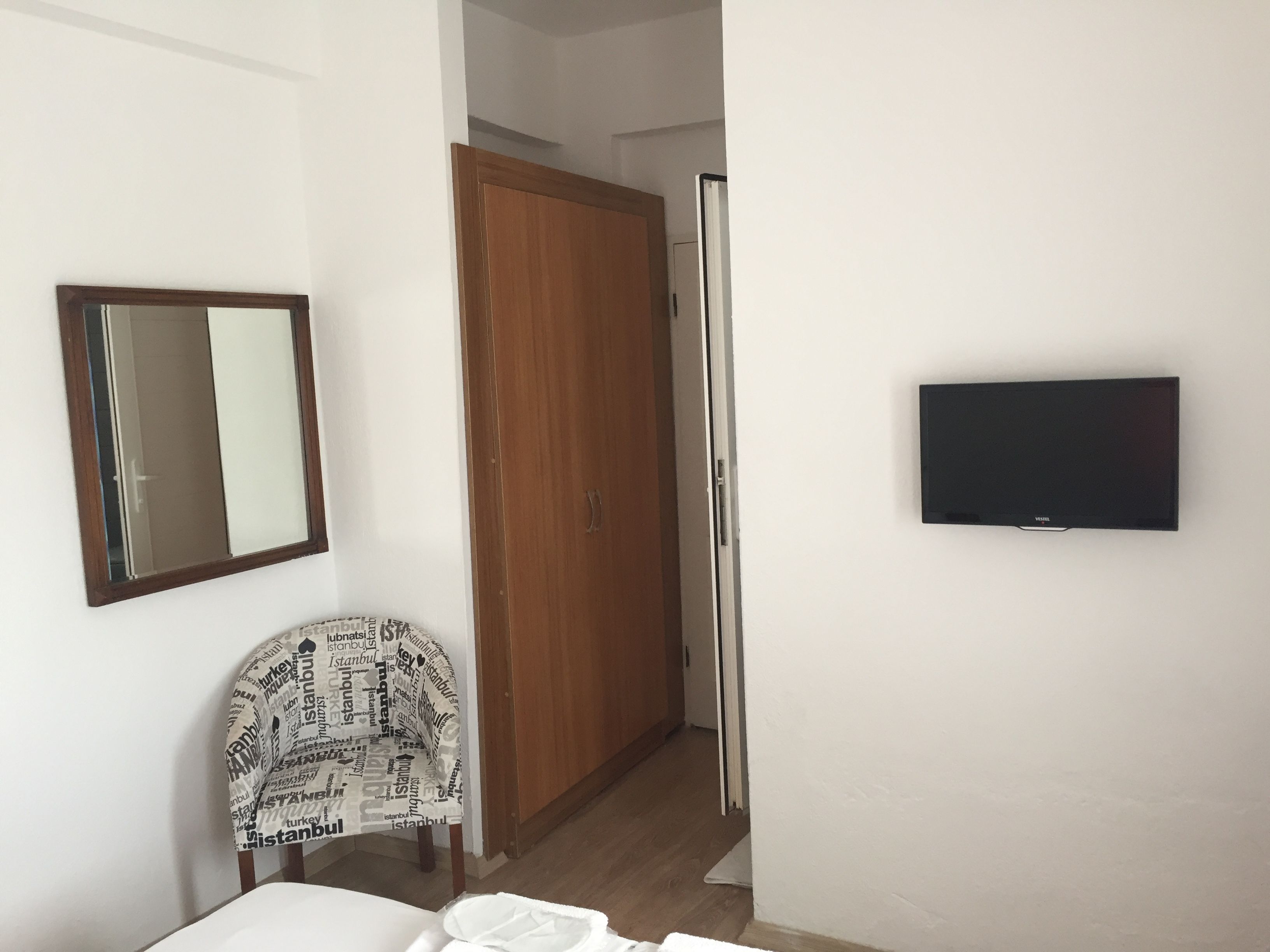 Una habitación con un armario de madera, un espejo, un televisor y una silla con un cubre acolchado estampado.