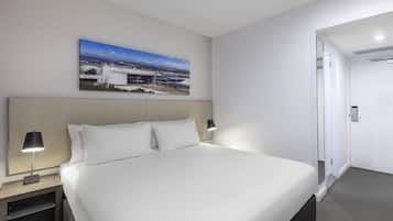 A modern hotel room with a large bed, a nightstand with a lamp, a painting on the wall, and a door leading to another room.