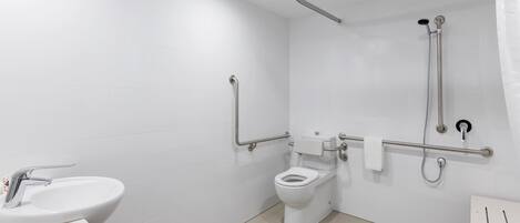 Casa de banho moderna com lavatório branco, sanita e zona de duche, equipada com barras de apoio e guarda-corpo.