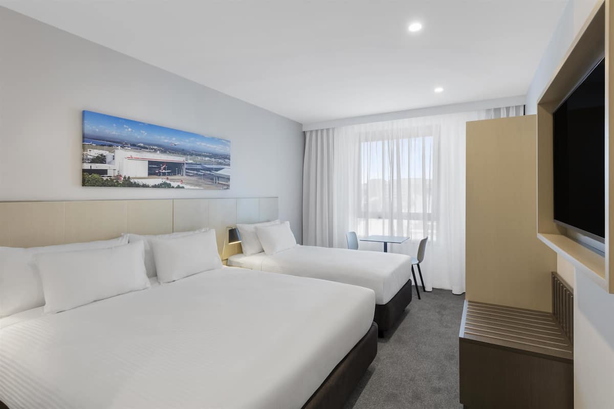 A hotel room with two beds, a television, a desk, and a window with curtains.