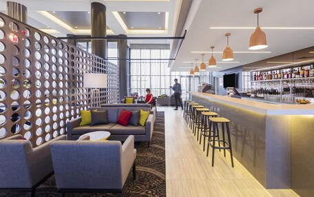 A modern hotel lobby with a bar area, seating arrangements, and a large window providing natural light.