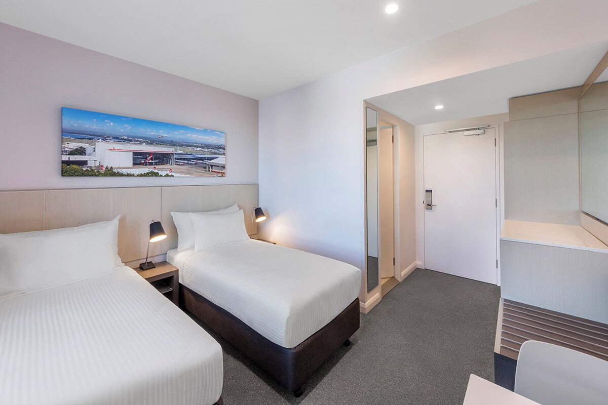 Une chambre d’hôtel avec deux lits, une grande fenêtre donnant sur la ville, un miroir et une porte menant à la salle de bain.