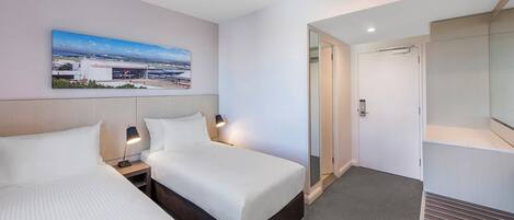 A hotel room with two beds, a large window with a cityscape view, a mirror, and a door leading to a bathroom.