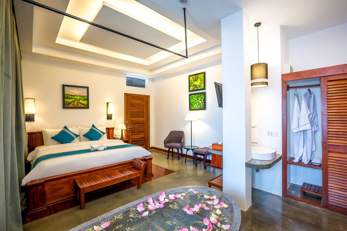 A hotel room with a bed, bedside tables, a desk, a chair, a vanity with a mirror, and a wardrobe.
