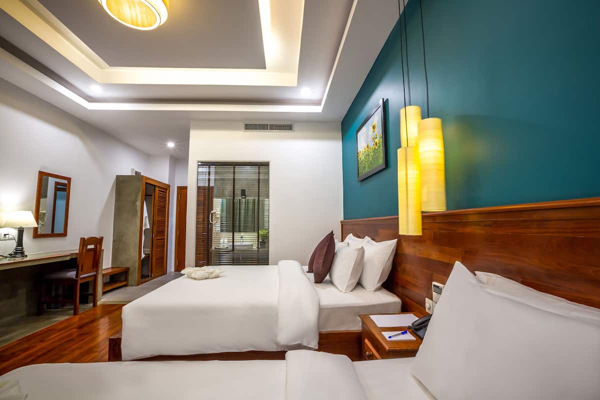 A hotel room with two beds, a desk, a chair, a lamp, and a painting on the wall.