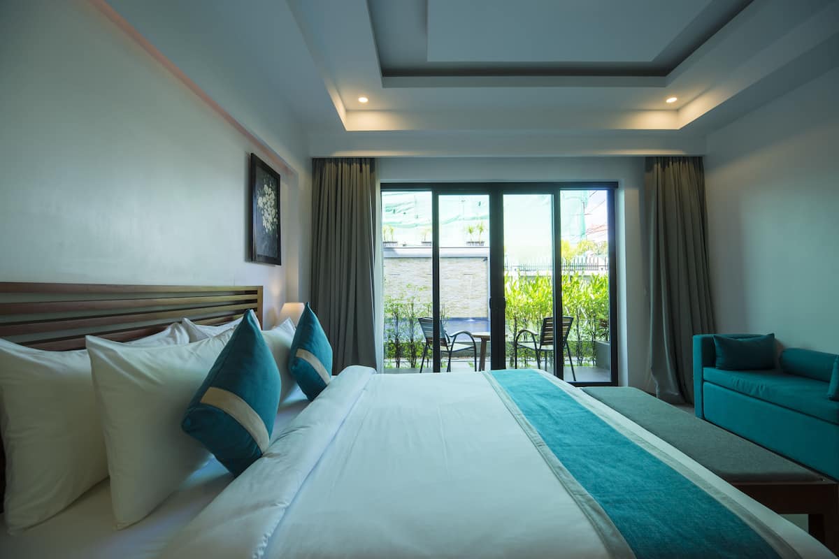 A hotel room with a large bed, a sofa, and a balcony with a view.