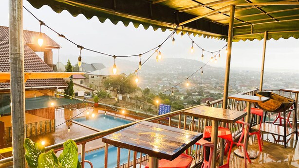 A rooftop terrace with a pool, tables, and chairs, overlooking a cityscape. - Triple Hill Hotel (Janman)