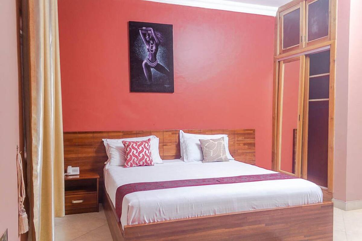 A bedroom with a wooden headboard, a bed with white and patterned pillows, a bedside table with a phone, and a painting on the wall.
