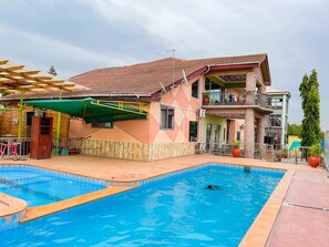 Una casa de dos pisos con piscina, un patio cubierto y un balcón.
