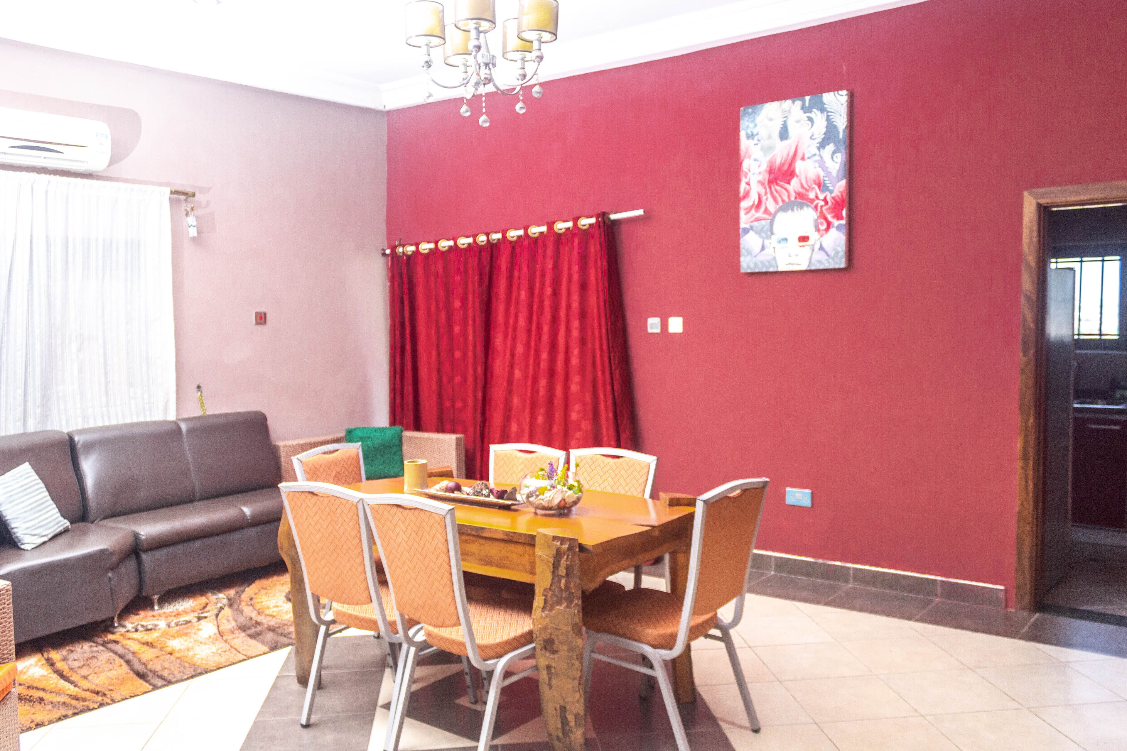 A living room with a sofa, a dining table with chairs, a red curtain, and a chandelier.