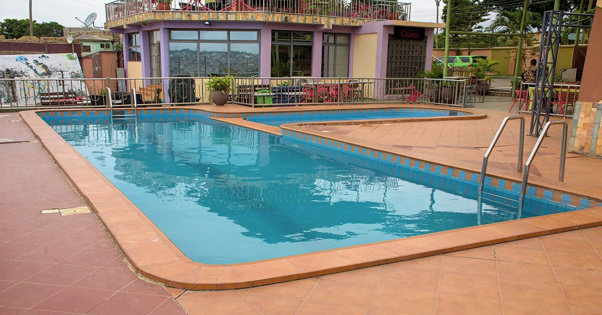 Una piscina con solárium empedrado y un edificio con balcón al fondo.