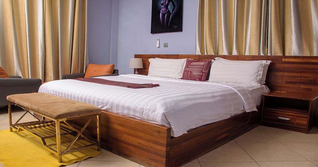 Een keurig opgemaakt slaapkamer met een houten bed, een bankje en een nachtkastje.