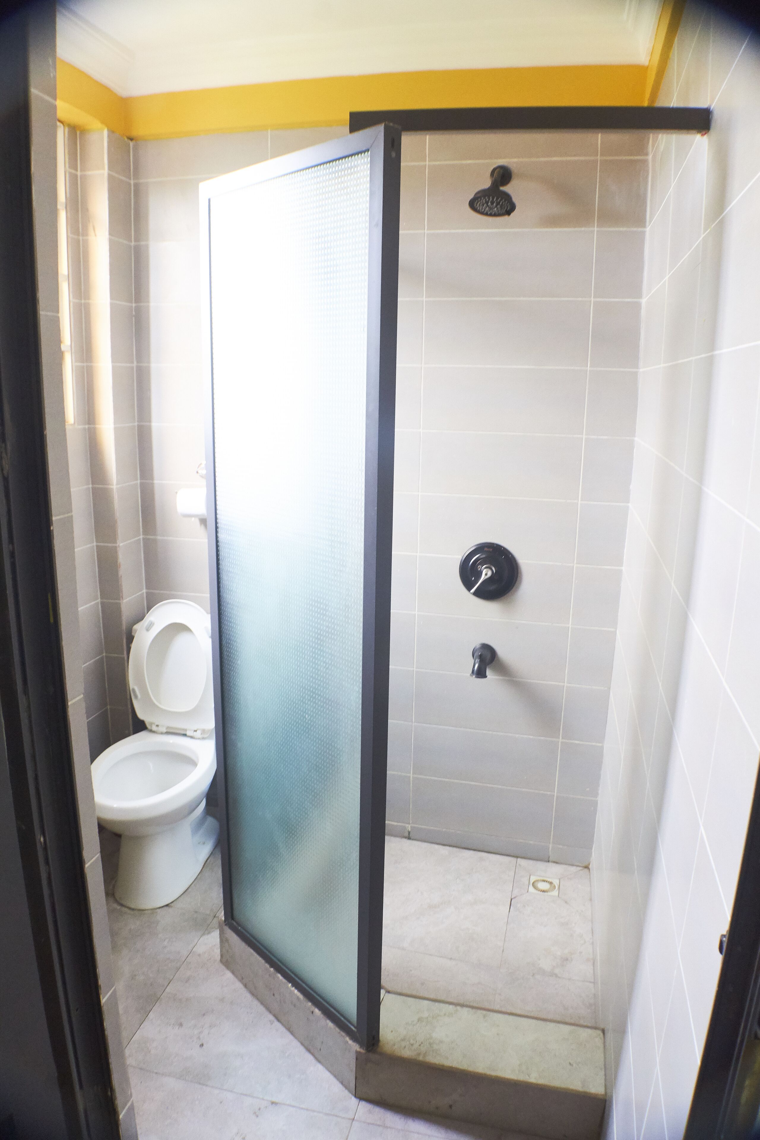 Un baño con inodoro, ducha con puerta de vidrio y paredes con azulejos.