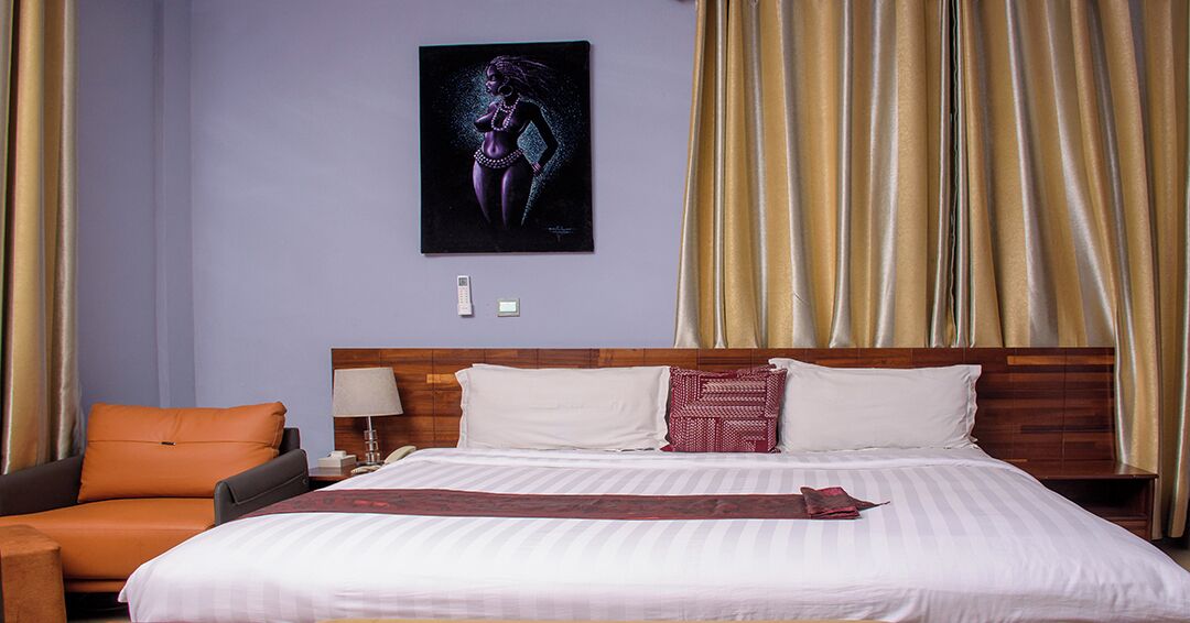Une chambre d’hôtel avec un grand lit, une table de chevet, une lampe, une chaise et un tableau au mur.