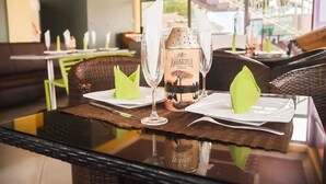 A dining area with wicker furniture, a glass table, and a bottle of Amarula liqueur. - Triple Hill Hotel (Janman)
