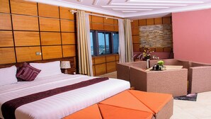 A hotel room with a large bed, a seating area with a table, and a view of the outdoors through a window. - Triple Hill Hotel (Janman)