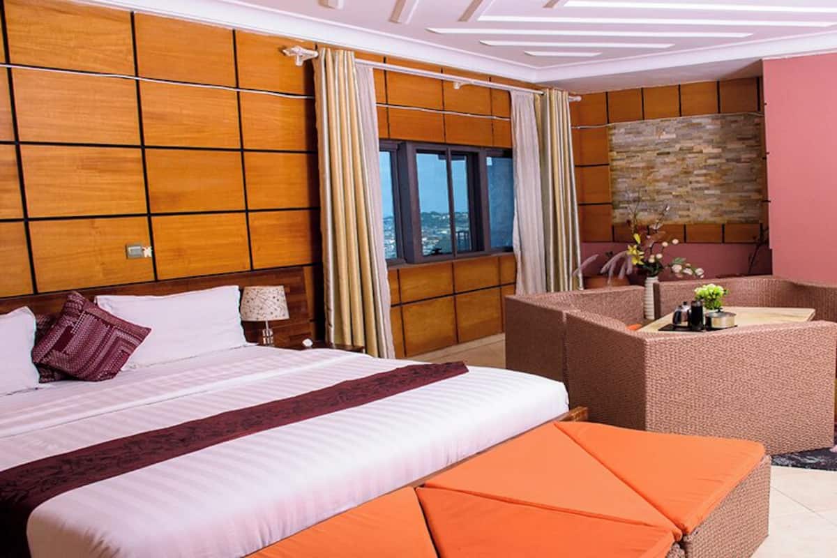 A hotel room with a large bed, a seating area with a table, and a view of the outdoors through a window.