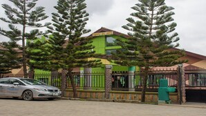 A building with a green and yellow facade, a gated entrance, and a car parked in front. - Triple Hill Hotel (Janman)
