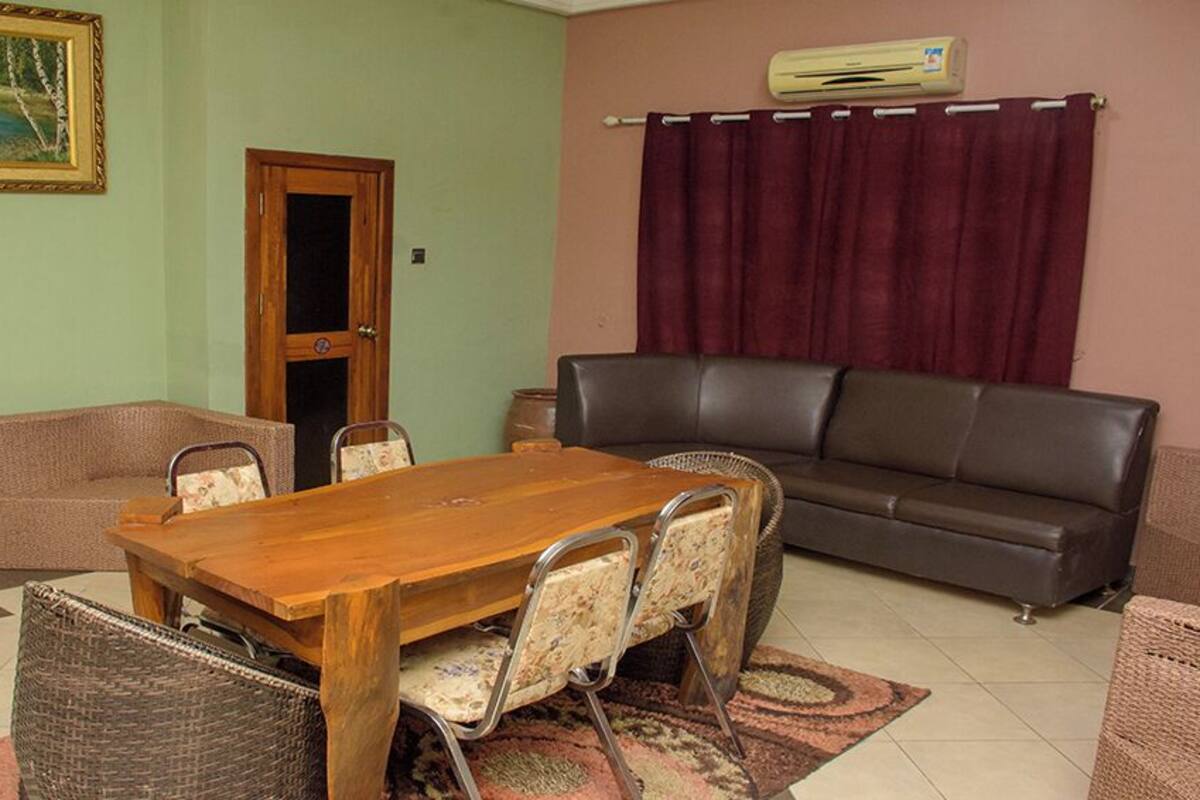 A dining area with a wooden table and chairs, a sofa, and a painting on the wall.