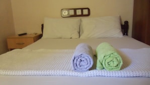 A neatly made bed with a white comforter and two rolled towels, one purple and one green, placed on the bed. - Pinara Pension & Guesthouse (Fethiye)