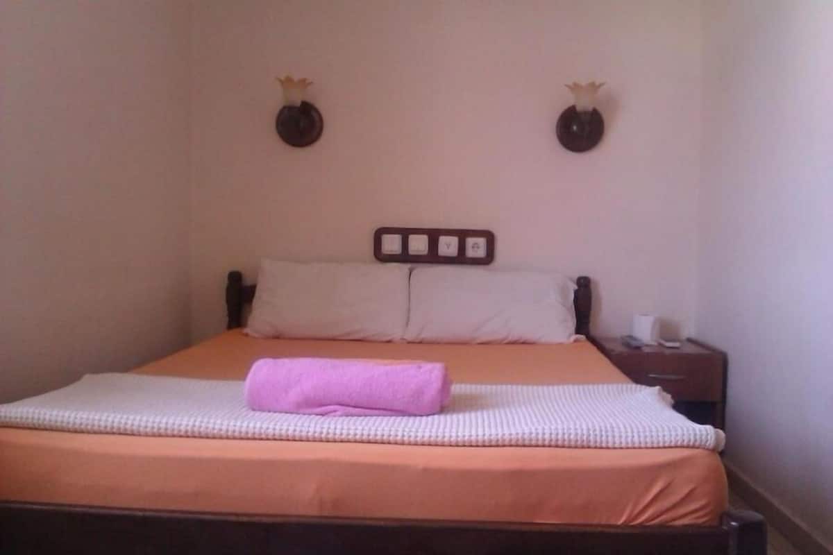A neatly made bed with a pink towel, a wooden headboard, and a small bedside table with a lamp.