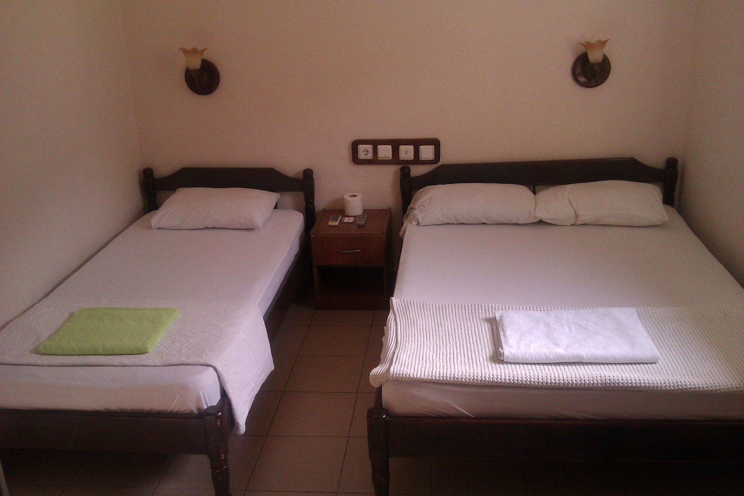 Two single beds with wooden frames, white bedding, and a small bedside table with a remote control and a tissue box.