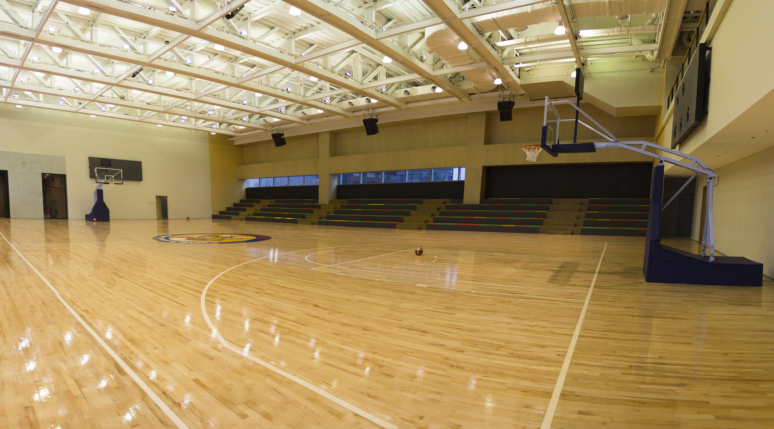 An indoor basketball court with a wooden floor, a basketball hoop, and a seating area with bleachers.