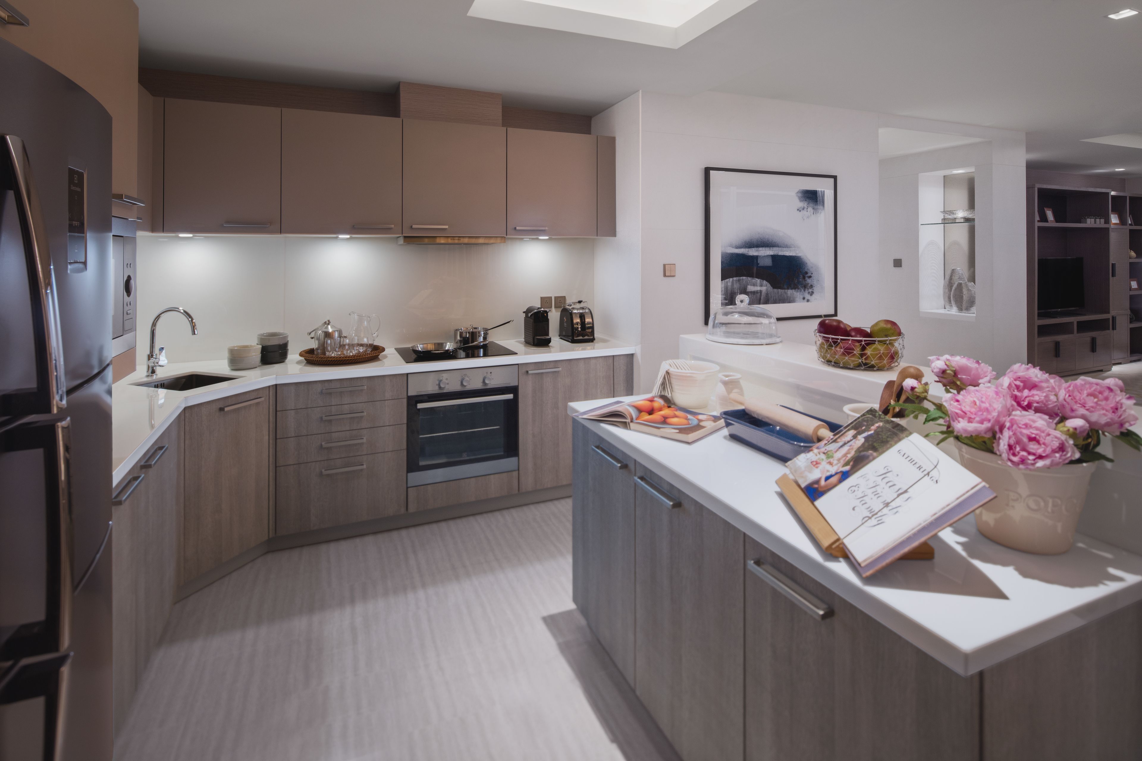 A modern kitchen with built-in appliances, a white countertop, and a dining area with a vase of flowers.