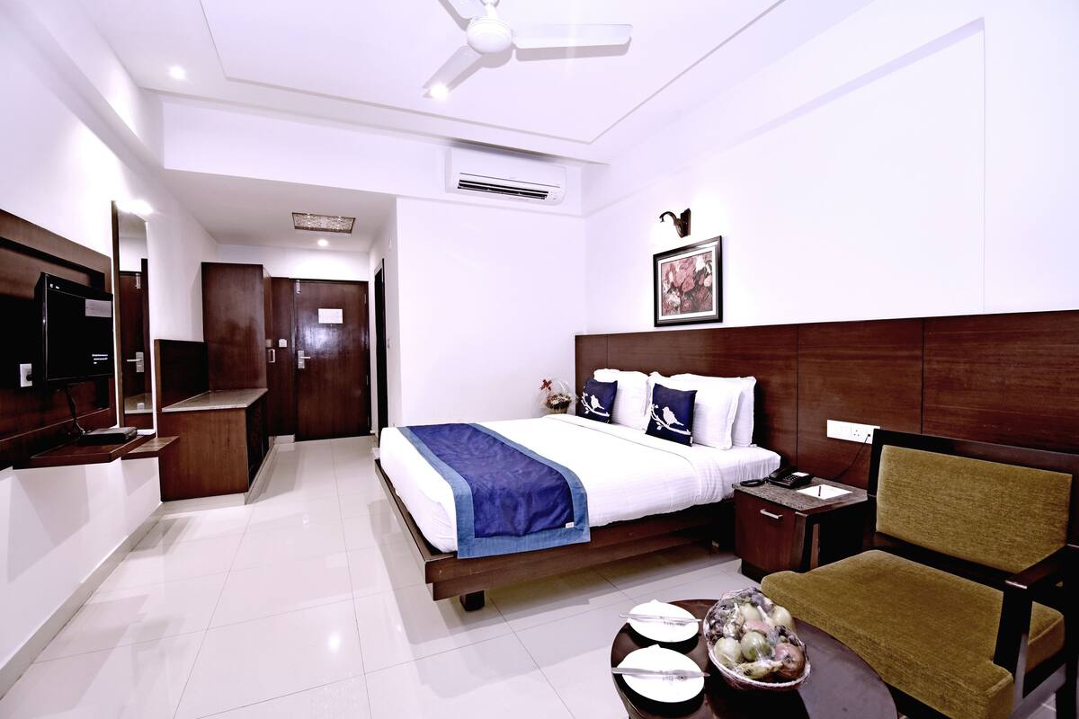 A hotel room with a bed, bedside table, chair, and a small dining area with plates and bowls.