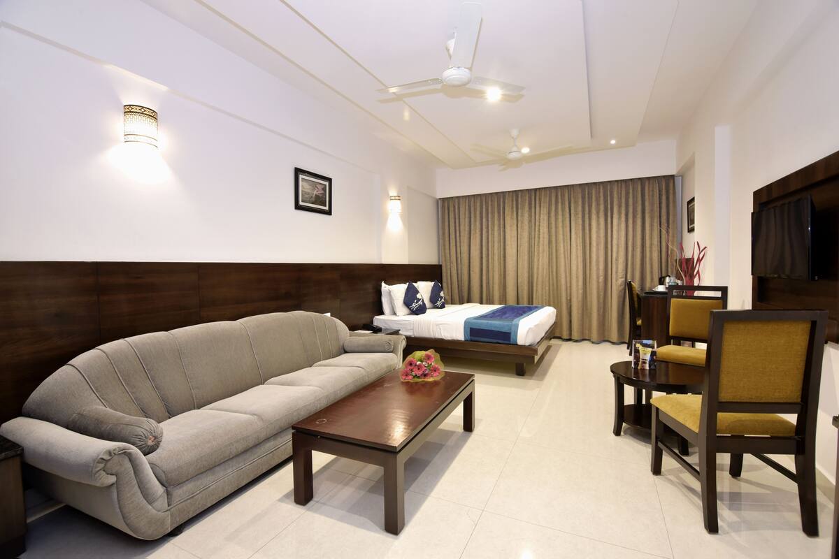 A hotel room with a sofa, a bed, a coffee table, a chair, a TV, and a ceiling fan.