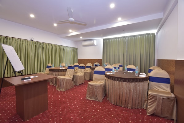 Une salle de conférence équipée d’une table ronde, de chaises, d’un tableau blanc et d’un ventilateur de plafond.