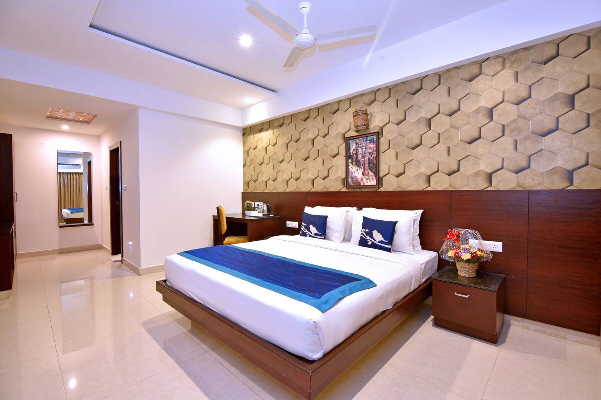 A modern hotel room with a large bed, a wooden headboard, a nightstand, and a ceiling fan.