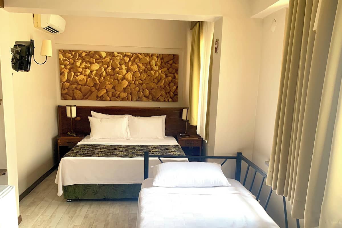 A hotel room with two beds, a stone wall decoration, a wooden headboard, and a small bedside table with a lamp.