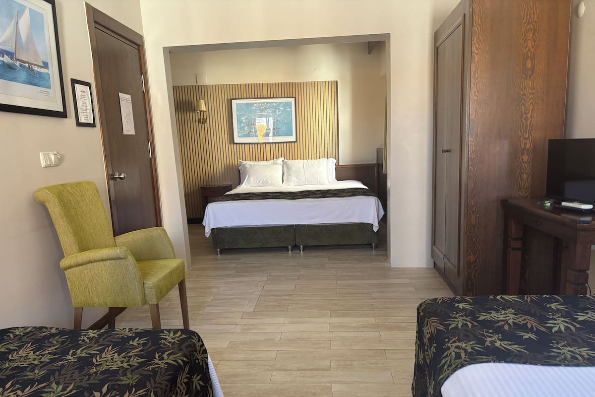 A hotel room with a bed, a green armchair, two bedside tables, a TV, and a framed picture on the wall.