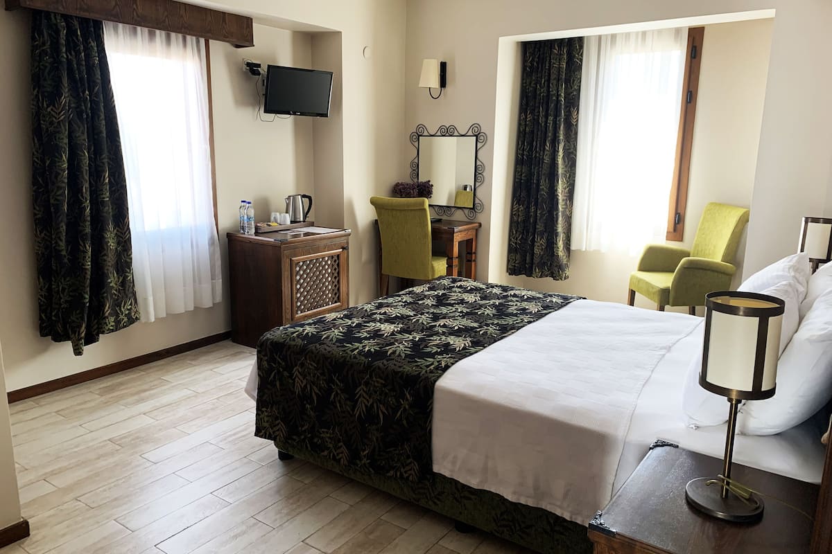A hotel room with a bed, a desk with a television, a chair, and a lamp.
