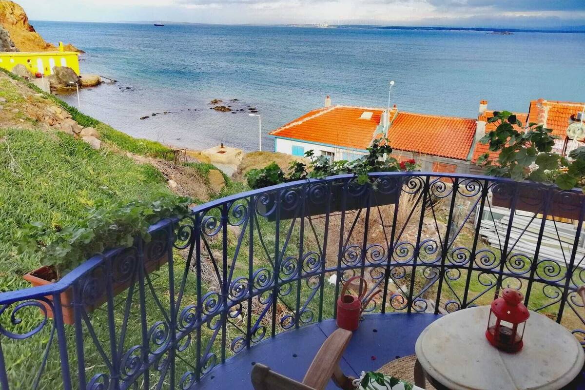 A balcony with a view of the sea, a red lantern, and a table with a chair.