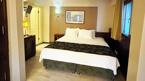 A hotel room with a bed, a bedside table, a lamp, a framed picture on the wall, and a window with curtains. - Mitos Hotel (Bozcaada)