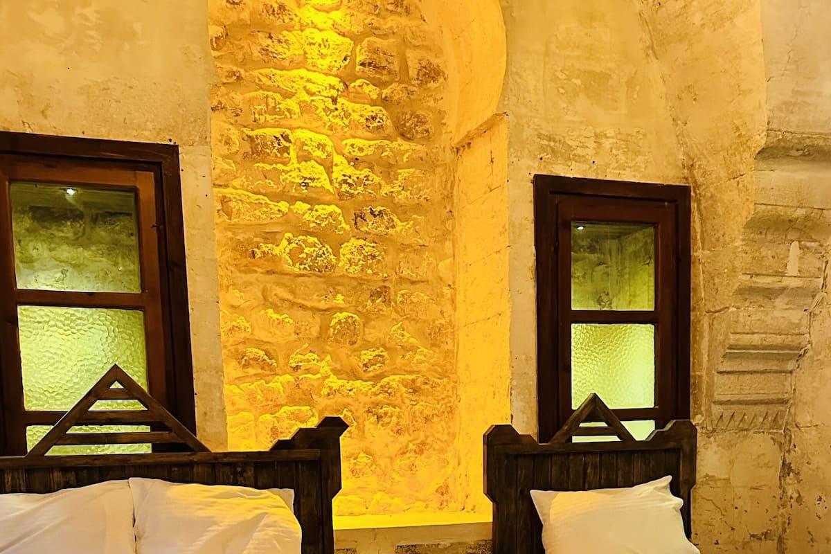 A room with two wooden beds, a stone wall, and a small window.