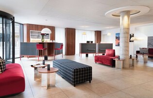 A modern hotel lobby with a bar, seating areas, and a large column.