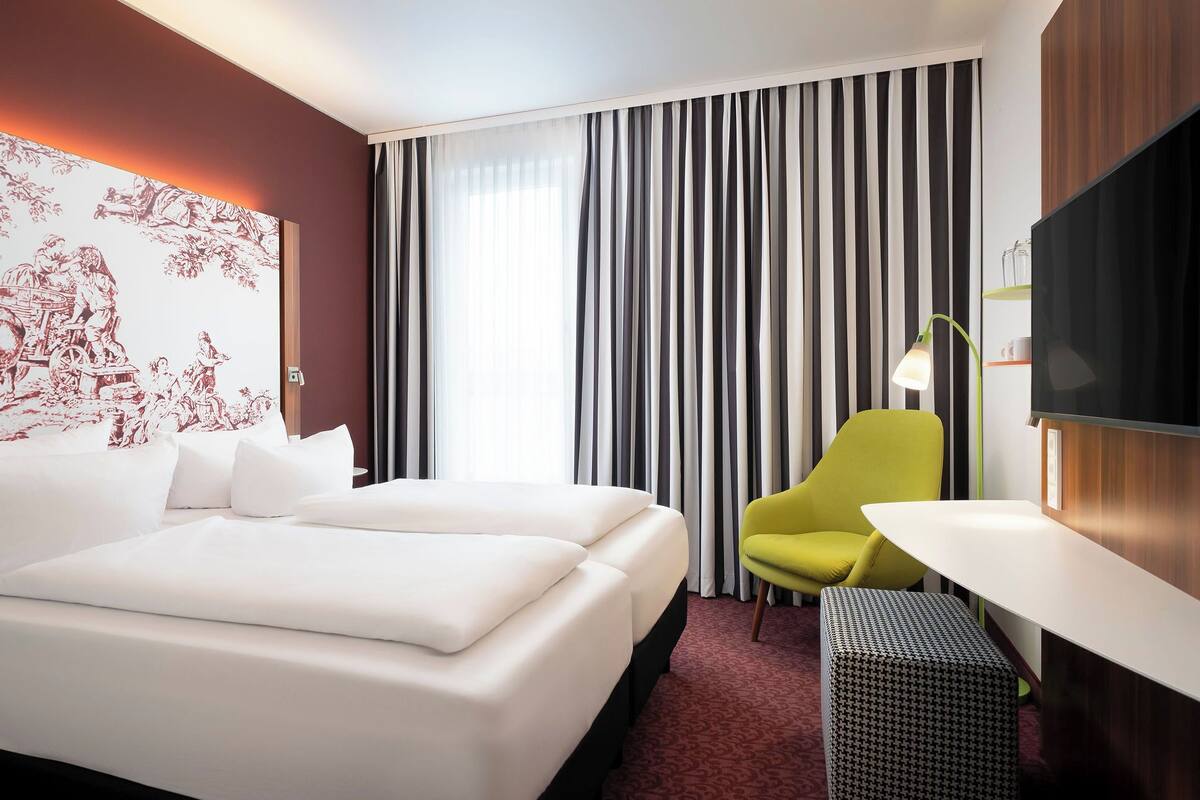 Habitación de hotel con cama, una silla, un televisor y una pared con un mural rojo y blanco.