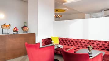 Un espace lounge moderne avec un canapé rouge recouvert de tissu, un comptoir d’accueil en bois agrémenté de corbeilles de fruits et un lustre.
