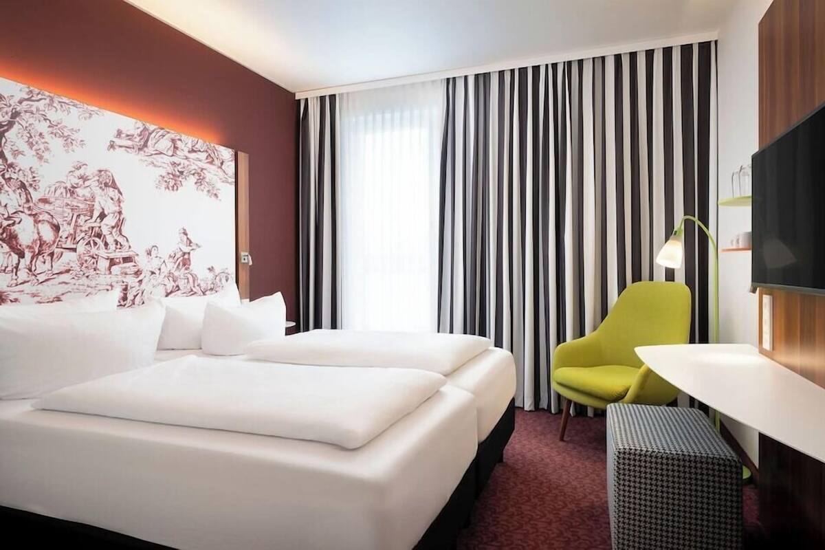 Una habitación de hotel con una cama grande, un escritorio, una silla, un televisor y una ventana con cortinas.