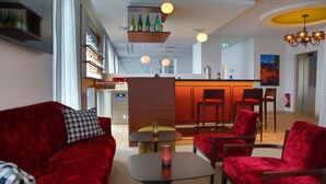 Eine Hotelhalle mit einer roten Samsofa, einem kleinen Tisch mit einer Dekoration und einem Barbereich mit roten Stühlen.