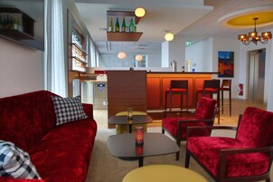 A hotel lobby with a red velvet sofa, a small table with a decorative item, and a bar area with red chairs.