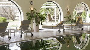 A sunlit indoor pool area with lounge chairs and a large potted plant. - Hotel Alpenhof Grainau (Grainau)
