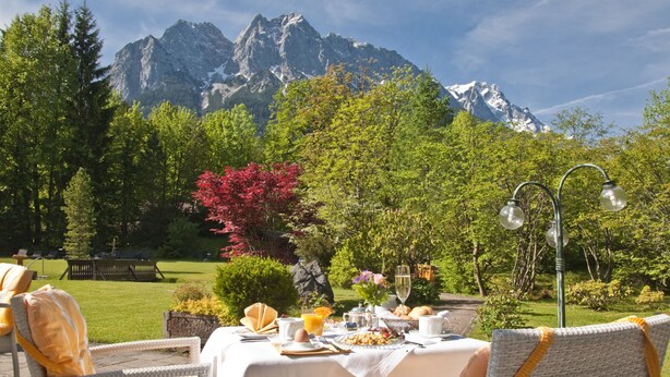 A table set for breakfast with a mountain view in the background. - Hotel Alpenhof Grainau (Grainau)