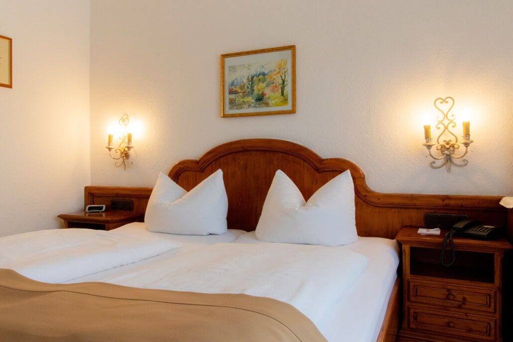 A hotel room with a wooden headboard, white bedding, two bedside tables with lamps, and a painting on the wall.