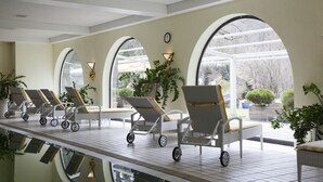 A sunlit indoor pool area with lounge chairs and potted plants. - Hotel Alpenhof Grainau (Grainau)