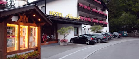 Un hotel con un letrero que dice "HOTEL Alpenhof" y una fila de coches estacionados adelante.